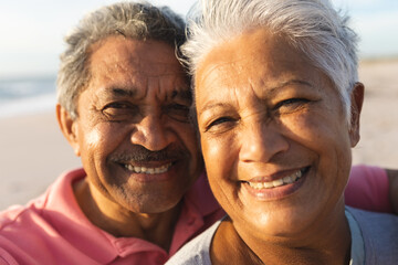 Close-up portrait of smiling multiracial senior couple with white hair enjoying sunset at beach