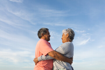 Smiling senior couple embracing, looking up against sky