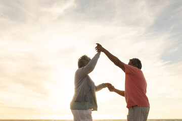Obraz premium Low angle side view senior multiracial couple enjoying dance at beach against sky during sunset