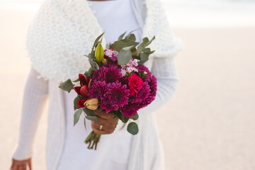 Midsection of senior woman holding fresh flowers bouquet at beach during sunset