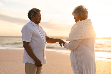 senior woman putting ring on bridegroom while standing at beach during wedding ceremony