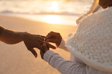 Obraz premium Midsection of senior bride putting ring on bridegroom's finger at beach wedding ceremony