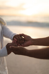 Cropped image of bridegroom holding hands of bride at beach during sunset