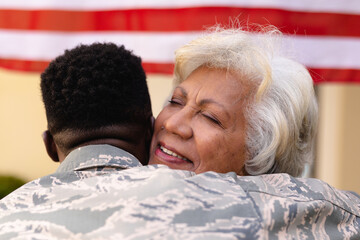Contented senior african american woman hugging military son outside house