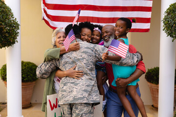 Happy african american family with usa flag hugging army soldier on his return home