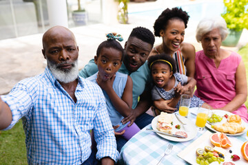 Portrait of three generational african american family taking selfie sitting at dining table