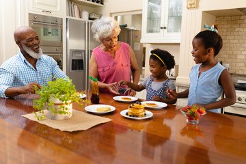 African american grandmother serving breakfast for two granddaughters in kitchen at home
