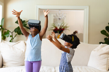 Two african american sisters wearing vr headset gesturing at home