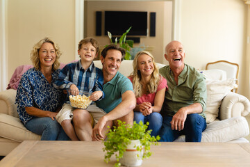 Caucasian three generation family watching tv sitting together on couch smiling at home