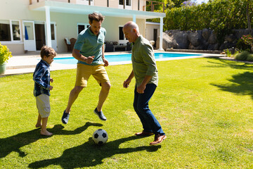 Caucasian grandfather, father and son playing football together in the garden