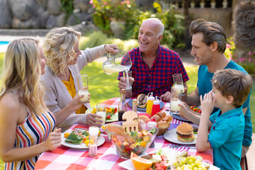 Cheerful caucasian three generational family enjoying lunch at table in garden