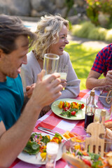 Cheerful caucasian senior woman sitting with family sitting together in garden during lunch