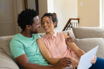 Happy young couple using laptop while sitting together on sofa at home