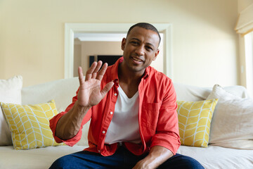 Portrait of smiling young african american woman waving during video call at home