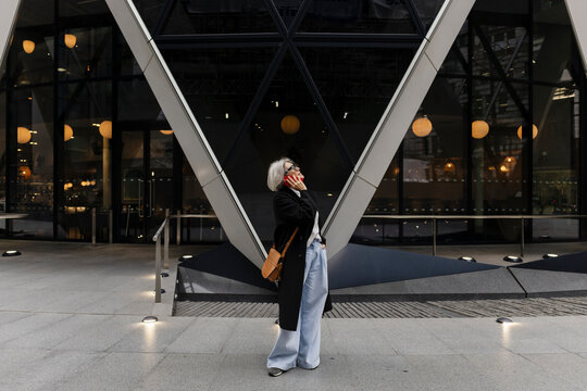 Stylish woman making phone call in front of modern building in London