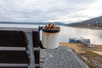 Cigarette butts in a metal ashtray on a bench in nature
