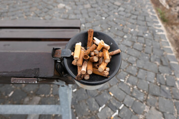 Cigarette butts in a metal ashtray on a bench in nature