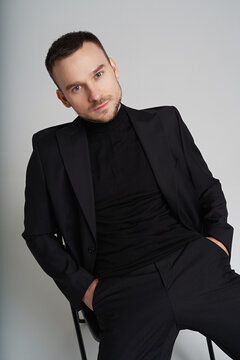 Portrait of man in classic black suit sitting in minimalistic studio