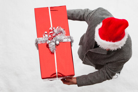 Person delivering Christmas present outdoors in snow with Santa hat