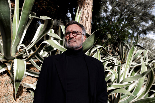 Elegant businessman in black trench coat standing among agave plants outdoors