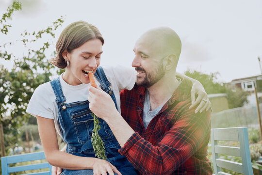 Smiling couple joking and gardening on allotment with fresh carrot