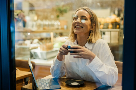 Smiling woman enjoying coffee and laptop at cafe with eye patch daytime