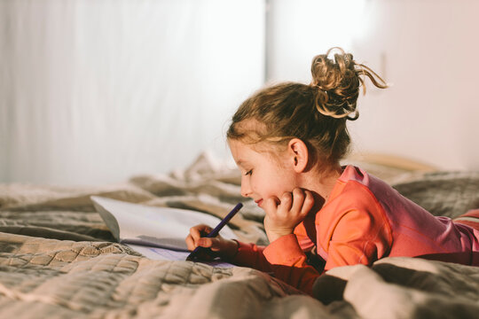 Child lying on bed drawing and enjoying creative quality time