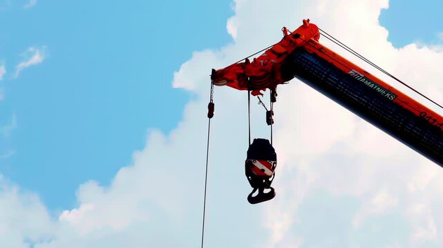 Industrial crane lifts load under blue sky with suspended hook and strong steel support frame, static detail