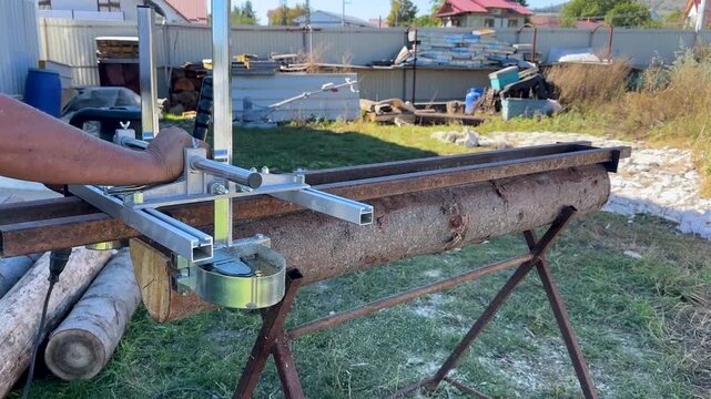 Video shows person using portable chainsaw mill attachment on large raw log outdoors, aluminum frame guide rail cutting slab