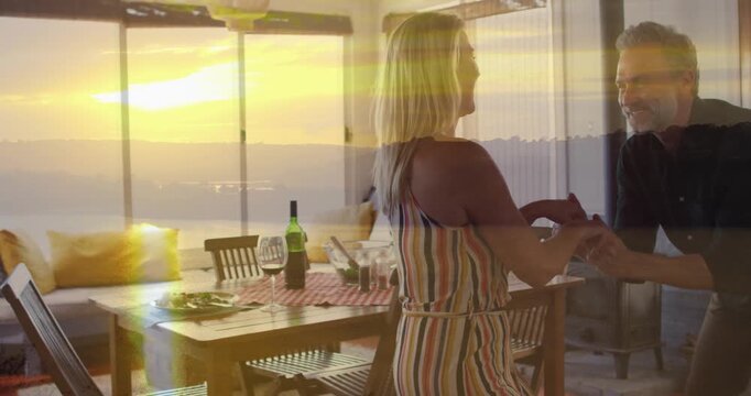 Dancing joyfully, couple enjoying sunset view over dining table at home