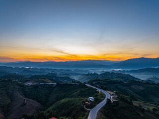 As dawn unfolds, sunlight spills over forested peaks, painting the sky in delicate gradients of orange and blue. The time lapse captures nature&rsquo;s quiet awakening in a serene mountain landscape.