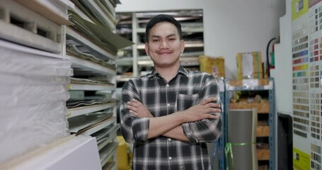 Asian adult male skilled worker stands confident, arms crossed beside wood material shelves inside construction supply store, presenting woodworking business owner identity in slow motion branding