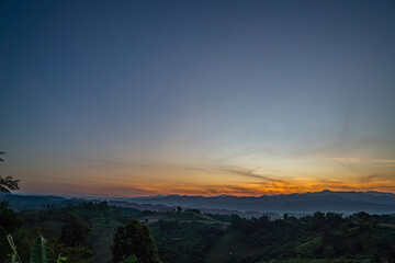 A breathtaking view of a colorful sunset over layered mountain silhouettes, with warm hues of orange, pink, and blue blending seamlessly across the sky.