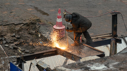 Industrial worker uses gas torch to cut steel beams during urban road construction and infrastructure repair, with sparks flying site