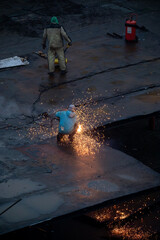 Two construction workers cutting metal sheets on an industrial site, creating bright sparks during heavy renovation or demolition work.