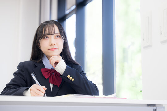 塾や学校、予備校などの教室で大学受験などの志望校の進路を悩む考える迷う、顎に手を当てる女の子　内申対策どうしようかな？