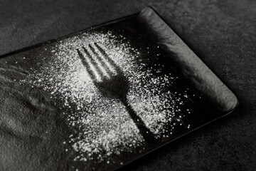 Imprint of a fork with powdered sugar on a black rectangular plate