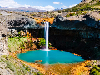 Majestic waterfall cascades into a vibrant turquoise pool surrounded by rugged, arid terrain with...