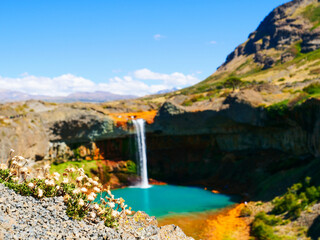 Captivating waterfall cascades into a vivid turquoise pool, framed by breathtaking multi-hued rock...
