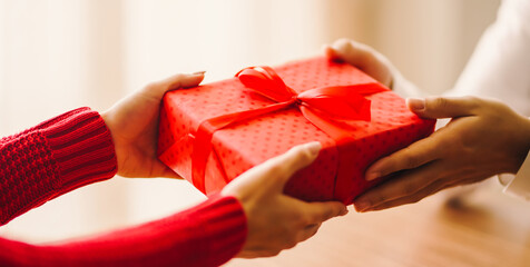 Close-up of a couple's hands exchanging a red gift on a sunny day. Surprise. Valentine's Day. A man gives a woman a gift in a cozy setting. Conceptually, it's about love, care, and celebration.