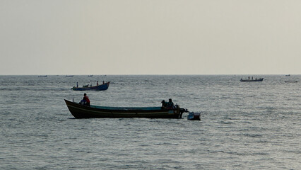 Obraz premium Silhouette of a small fishing boat on calm sea at dusk.