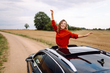 A happy woman leans out the car window, feeling free and enjoying the fresh air at sunset. A...
