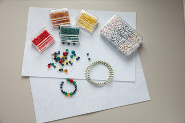 Jewelry making supplies with colorful glass beads, letter beads, and a handmade bracelet on white felt. Creative DIY hobby workplace for beading and craft projects.