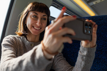 A happy woman takes photos on a train with her smartphone. She creates content for social media.