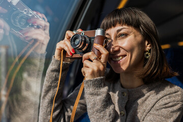 A beautiful, happy young woman takes a photo with a vintage analog camera from a train window. Concept of travel and discovery.