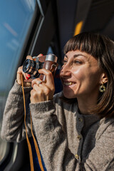 A happy young woman takes photos from a train window. The tourist creates content for social media. The concept of travel and discovery.