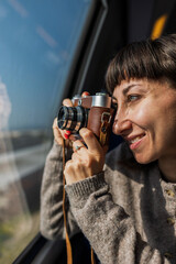 A beautiful, happy young woman takes a photo with a vintage analog camera from a train window. Concept of travel and discovery.