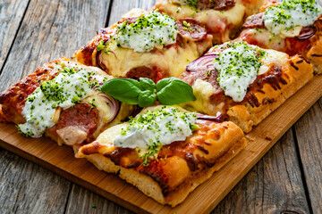 Pizza with sausage, mozzarella cheese, tomato sauce, red onion and broccoli yogurt on wooden table	