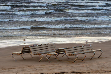 Empty beach chairs on Jurmala shore with waves crashing under cloudy sky