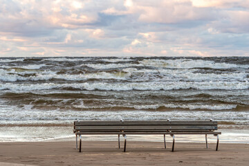 Empty beach chairs on Jurmala shore with waves crashing under cloudy sky